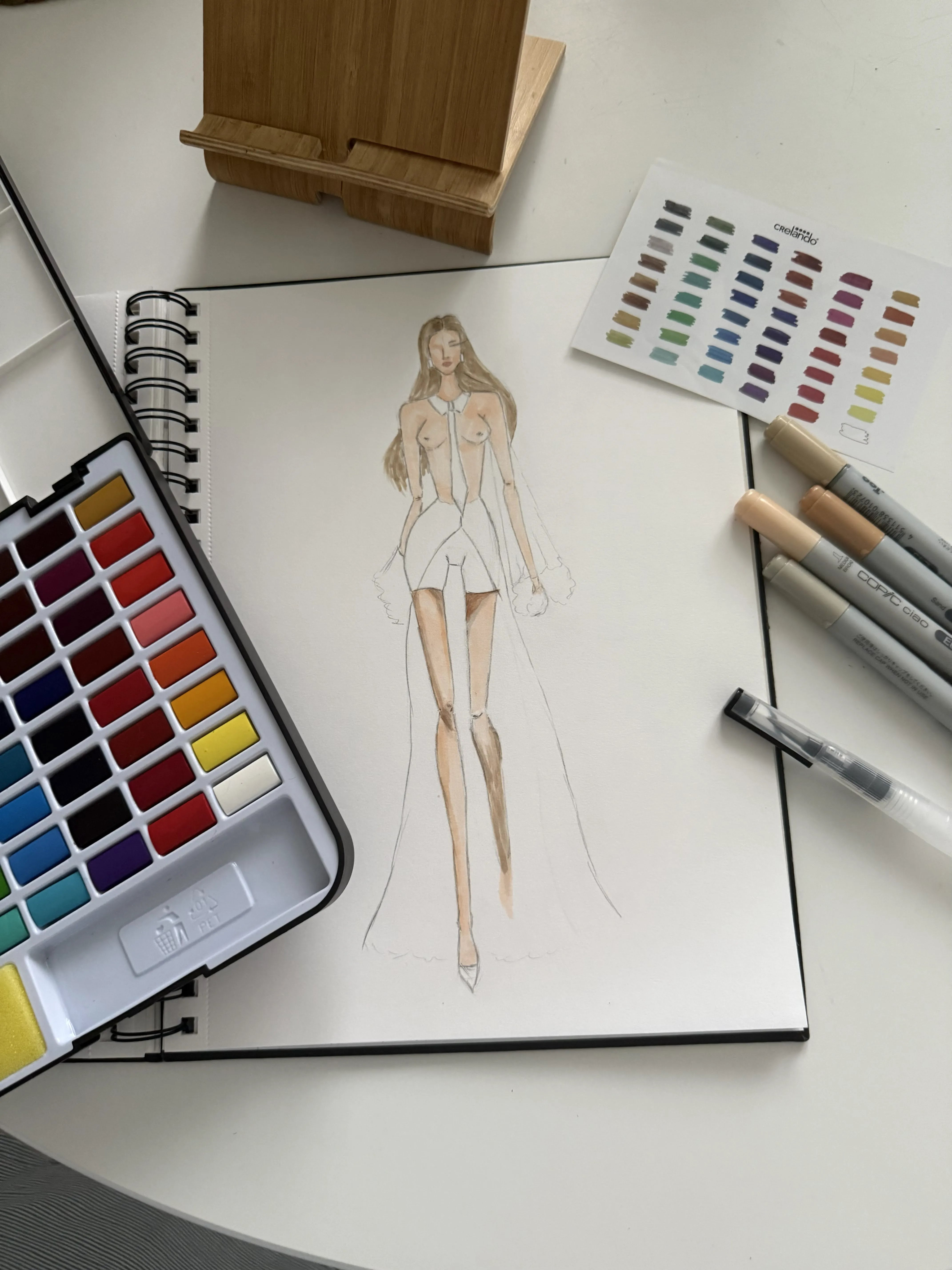 A fashion illustration in a sketchbook with drawing materials